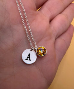 Silver-tone necklace with a pendant set with a yellow stone and an A initial.